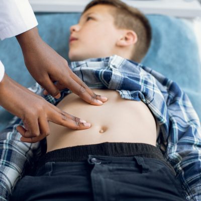 Child physical examination concept. Unrecognizable African American doctor performing manual palpation. Female pediatrician or health care practitioner examines little boy abdomen.